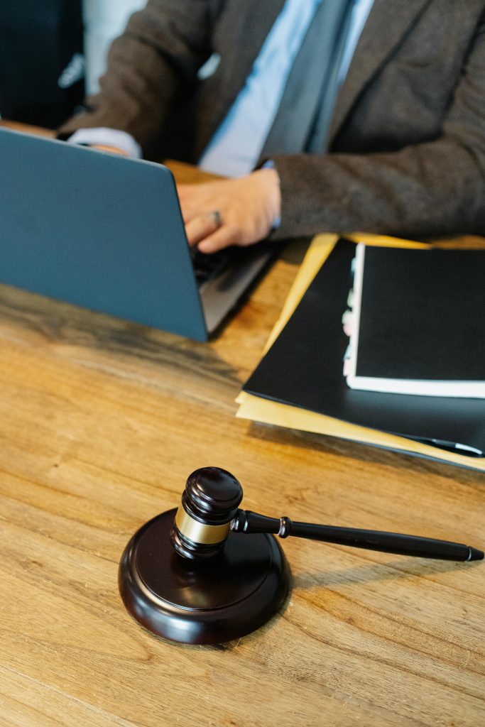 pexels-photo-5668802-5668802 From above of crop anonymous male lawyer in formal clothes typing on laptop while sitting at wooden table with stack of documents and gavel