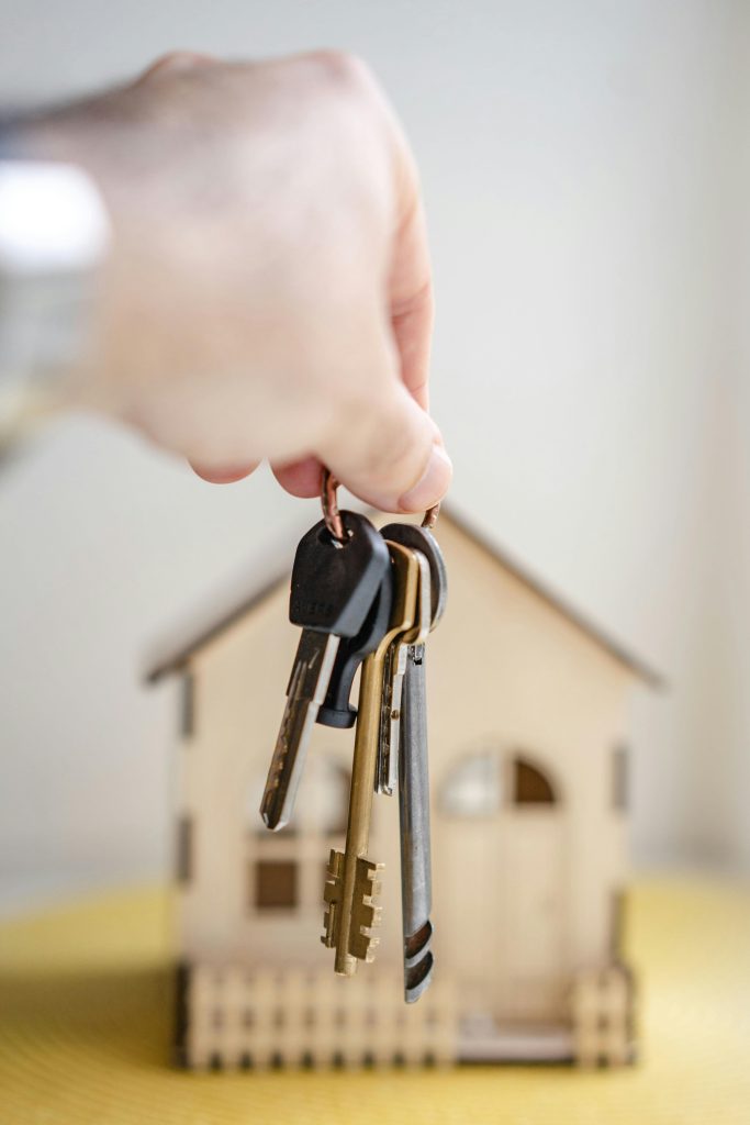 pexels-photo-7599735-7599735 Close-up of a hand holding keys with a miniature wooden house in the background, symbolizing real estate investment.